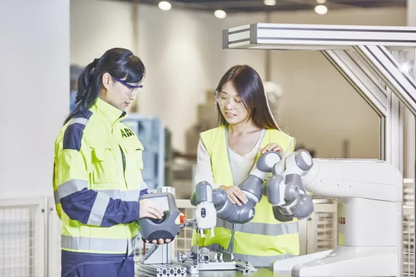 2 tjejer i varselkläder demonstrerar hur en yumi ABB cobot fungerar från JE robotteknik och automation
